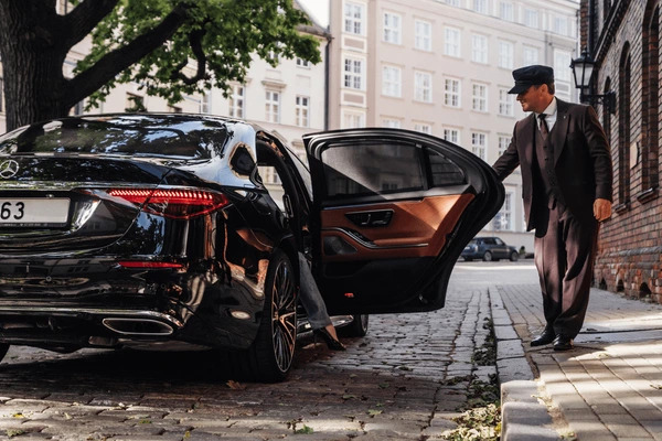 Chauffeur in uniform opening the rear door of a black luxury sedan
