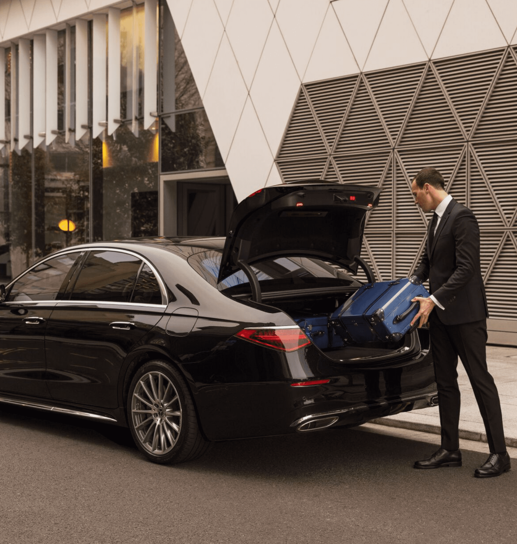 Chauffeur loading a suitcase into the trunk of a black sedan